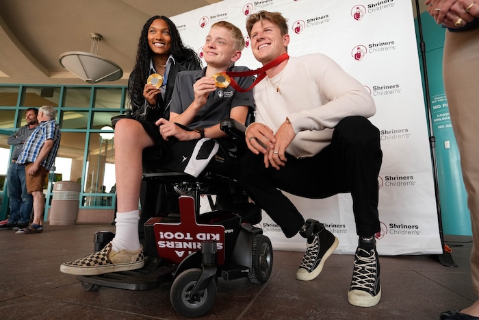 (Francisco Kjolseth  | The Salt Lake Tribune) Travis Carpenter, 17, poses for a photograph with Tara Davis-Woodhall and Hunter Woodhall, both gold medalists in the Paris 2024 Games, during a visit to Shriners Children’s Hospital on Wednesday, Sept. 18, 2024. Woodhall had his legs amputated when he was 11 months old and spent much of his youth at the hospital.