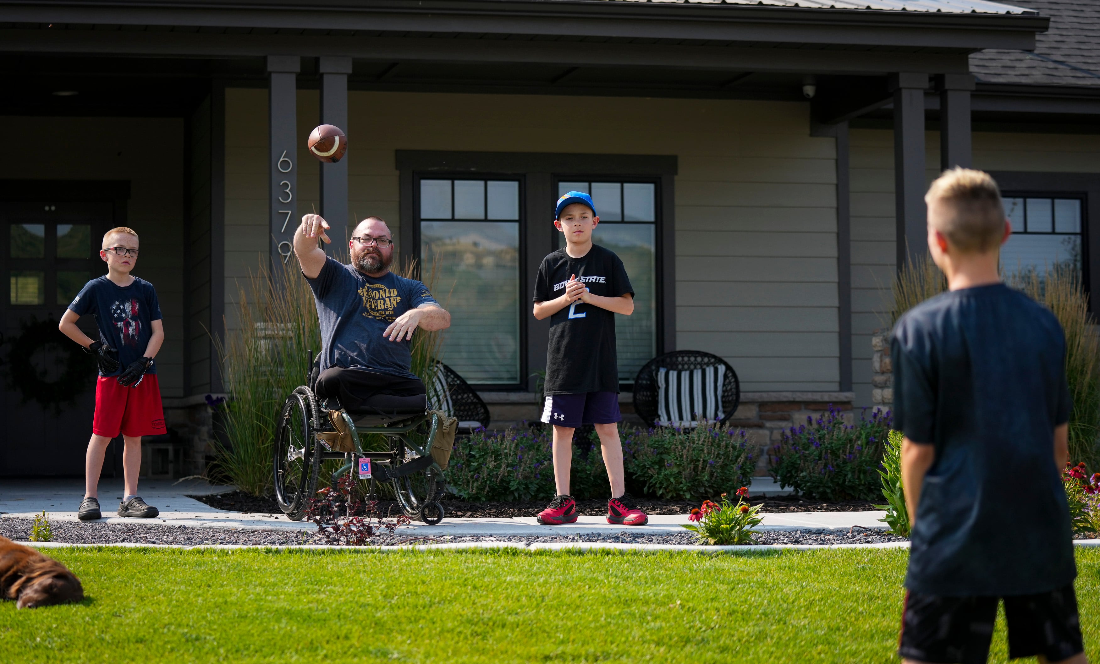 (Bethany Baker | The Salt Lake Tribune) Travis Vendela throws a football to his son Quentin as his other sons Kaiden, left, and Trayden, right, stand beside him outside their home in Huntsville on July 23, 2024. Travis was an enlisted Army reconnaissance unit leader when his vehicle drove over an improvised explosive device in Iraq in 2007. 
