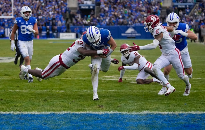 (Bethany Baker  |  The Salt Lake Tribune) Brigham Young Cougars quarterback Jake Retzlaff (12) runs the ball for a touchdown as Oklahoma Sooners defensive lineman R Mason Thomas (32) tackles him at LaVell Edwards Stadium in Provo on Saturday, Nov. 18, 2023.