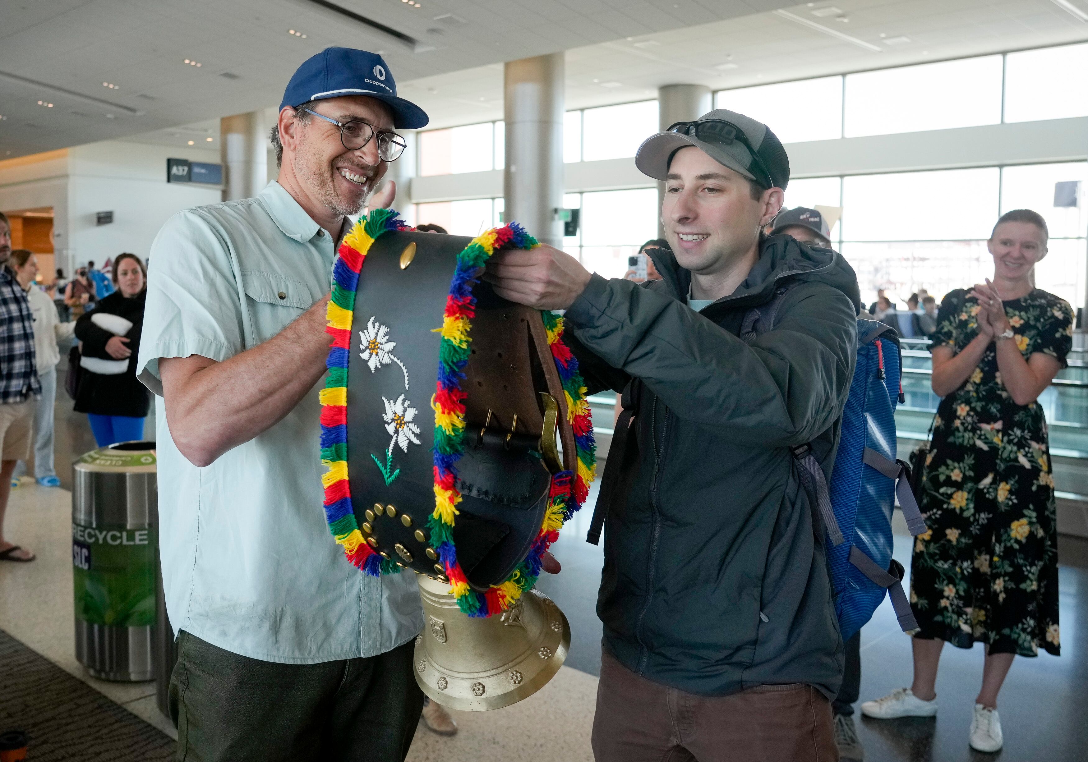 (Bethany Baker | The Salt Lake Tribune) Shawn Marquardt, left, the vice president of sales for the ski lift manufacturer Doppelmayr, hands a ceremonial cow bell to Peter Landsman during a surprise celebration for Landsman, the author behind Lift Blog, after he completed a lifelong goal of visiting each of the more than 3,000 ski lifts in North America as he travelled through Salt Lake International Airport in Salt Lake City on Saturday, June 22, 2024.