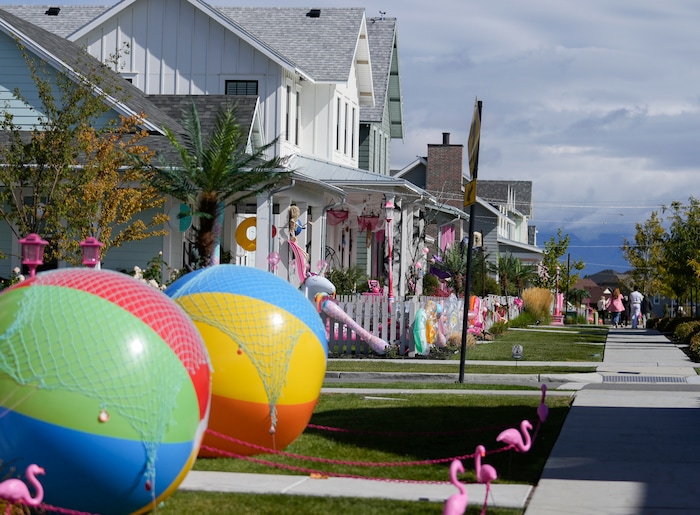 (Bethany Baker  |  The Salt Lake Tribune) People walk along a path between homes in a section of Daybreak that has collectively created a Barbieland-themed community for Halloween on Wednesday, Oct. 11, 2023.