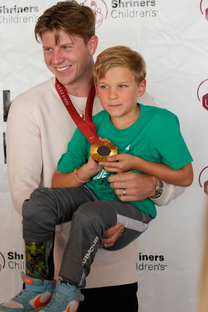 (Francisco Kjolseth  | The Salt Lake Tribune) Hunter Woodhall, a gold medalists in the Paris 2024 Games, picks up Zach Adler, 8, for a picture, just like he did when Zach was 1, during a follow up visit to Shriners Children’s Hospital on Wednesday, Sept. 18, 2024. Woodhall had his legs amputated when he was 11 months old and spent much of his youth at the hospital.