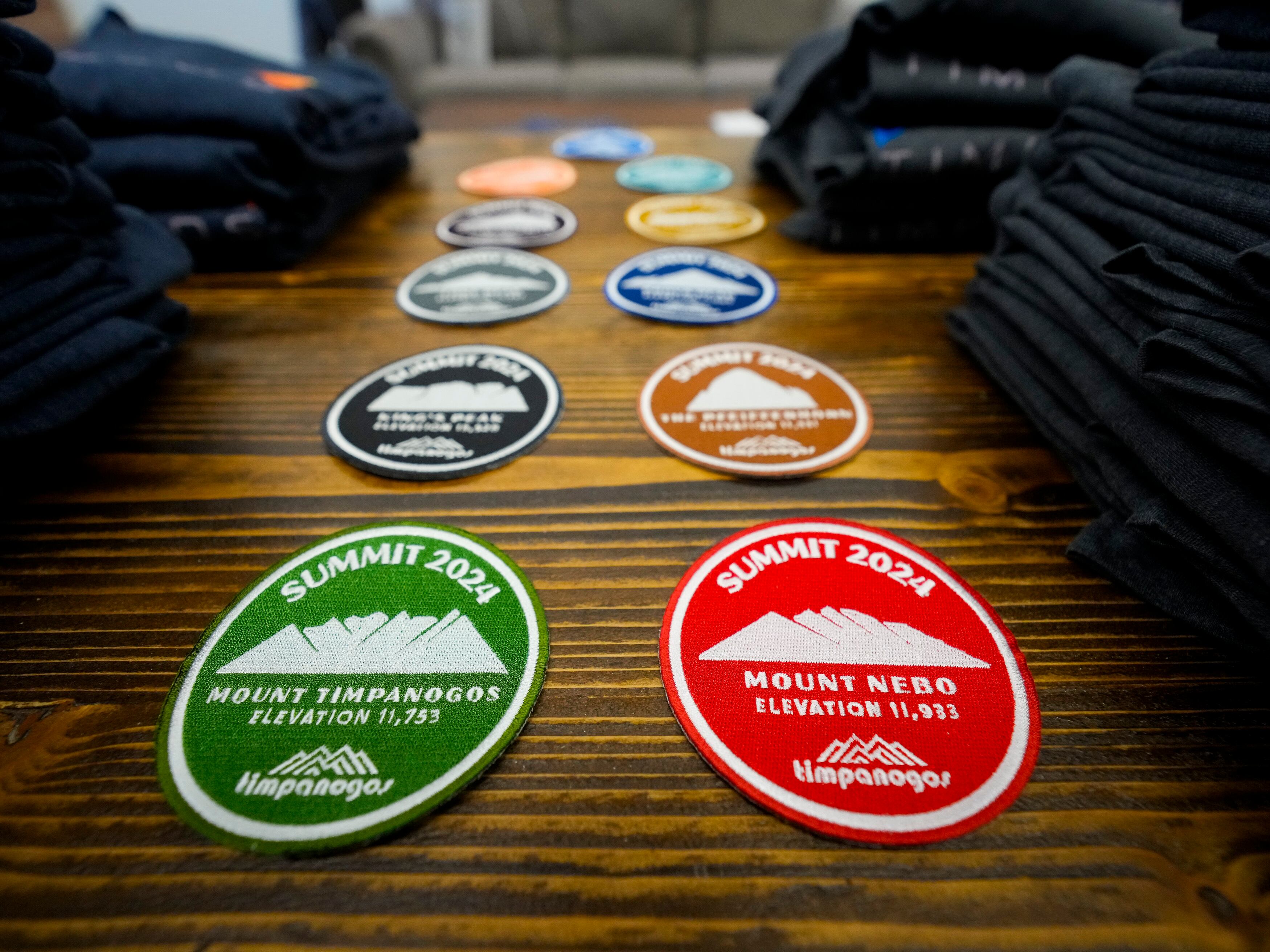 (Bethany Baker | The Salt Lake Tribune) Badges commemorating several Utah mountain peaks sit on a table at Timpanogos Hiking Co. in Provo on Wednesday, May 8, 2024. The hiking store offers these badges to hikers who post photos from the summit of each peak.