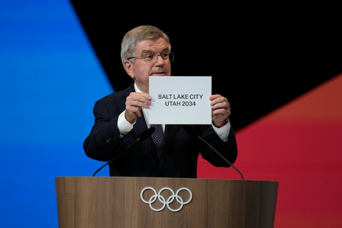 (Natacha Pisarenko | AP) IOC president Thomas Bach holds the board Salt Lake City during the 142nd IOC session at the 2024 Summer Olympics, Wednesday, July 24, 2024, in Paris. Salt Lake City was confirmed as host for the 2034 Winter Games by International Olympic Committee.