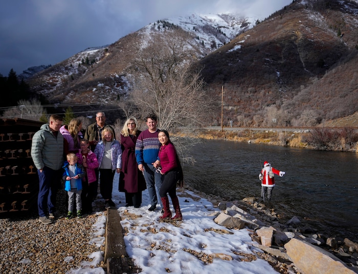 (Bethany Baker  |  The Salt Lake Tribune) A family takes a photo with Rudy Schenk, a fly fisherman dressed as Santa Claus, behind them at Vivian Park in Provo Canyon on Saturday, Dec. 23, 2023.