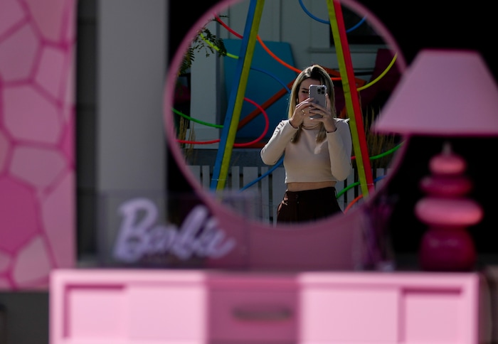 (Bethany Baker  |  The Salt Lake Tribune) A woman’s reflection is seen in the mirror of a vanity on a porch as she takes a photo of a home in a section of Daybreak that has collectively created a Barbieland-themed community for Halloween on Wednesday, Oct. 11, 2023. 