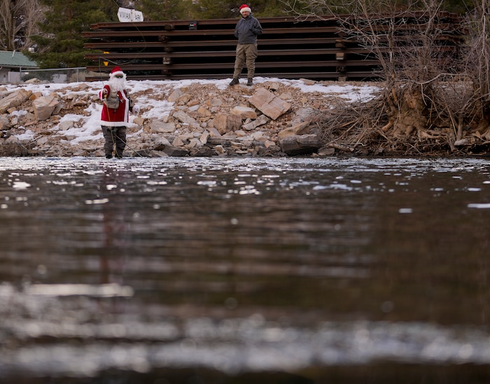 (Bethany Baker  |  The Salt Lake Tribune) Brett Prettyman stands on the bank as Rudy Schenk, a fly fisherman dressed as Santa Claus, casts his line in Provo River at Vivian Park in Provo Canyon on Saturday, Dec. 23, 2023.