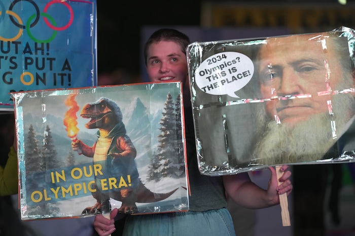 (Rick Egan | The Salt Lake Tribune) Eden Bingham holds signs during a live stream at Salt Lake City Hall of the vote to host the 2034 Winter Olympics, on Wednesday, July 24, 2024.