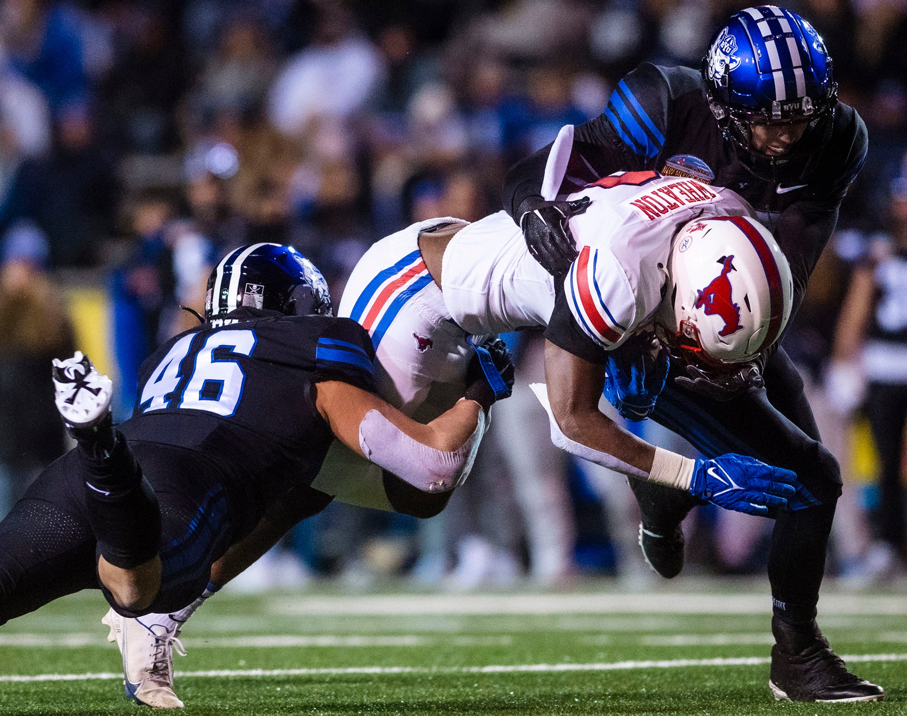 SMU's Camar Wheaton, center, is tackled by BYU's Logan Pili (46) and Matthew Criddle, right, during the first half of the New Mexico Bowl NCAA college football game in Albuquerque, N.M., Saturday, Dec. 17, 2022. (Chancey Bush/The Albuquerque Journal via AP)