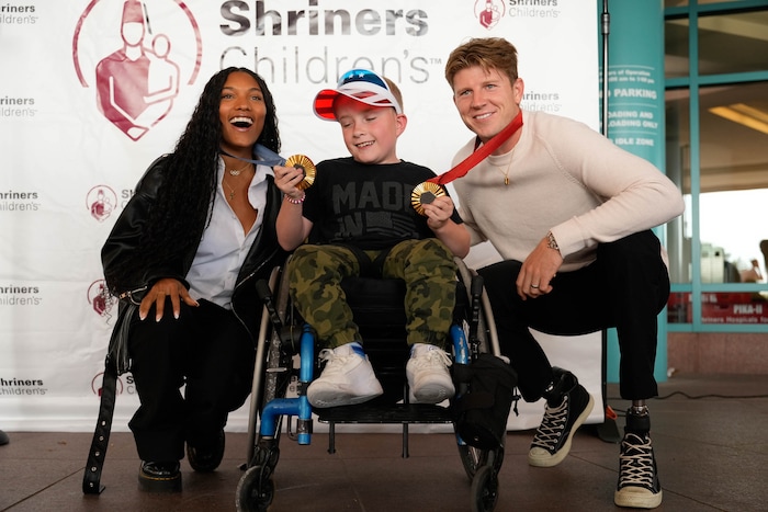 (Francisco Kjolseth  | The Salt Lake Tribune) Cole Spencer, 10, poses for a photograph with Tara Davis-Woodhall and Hunter Woodhall, both gold medalists in the Paris 2024 Games, during a visit to Shriners Children’s Hospital on Wednesday, Sept. 18, 2024. Woodhall had his legs amputated when he was 11 months old and spent much of his youth at the hospital.