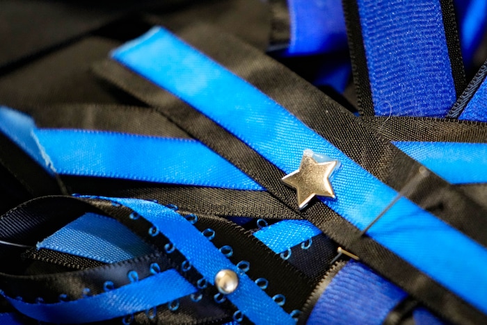 (Francisco Kjolseth  |  The Salt Lake Tribune) Pins are provided for those arriving for funeral services for Santaquin police Sgt. Bill Hooser at the UCCU Center at Utah Valley University on Monday, May 13, 2024.