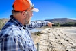 (David Condos | KUER) Coby Hunt points across the dam that diverts water from the Green River into the irrigation canal that runs by his field, Aug. 19, 2024. Because he’s been paid to fallow that land, the water he would typically use on his crops has been returning to the Green River downstream.